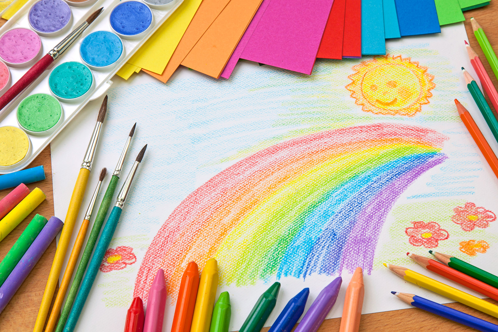Ein gezeichneter Regenbogen und Sonne mit darumliegenden Malutensilien