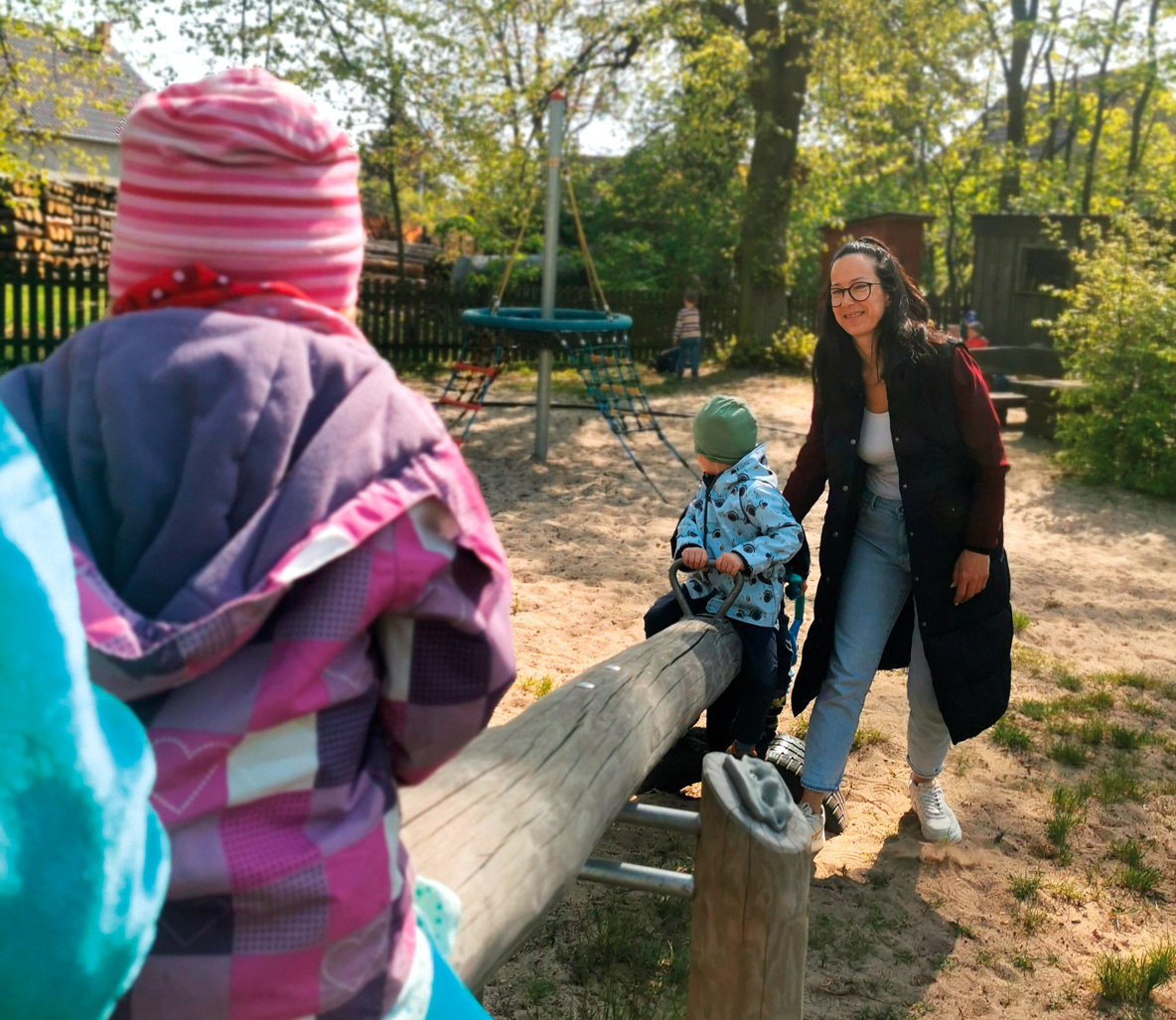 Kinder wippen mit einer Erzieherin auf dem Spielplatz des Kinderhauses Lütte