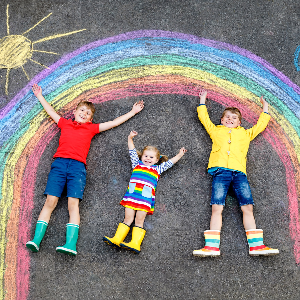 Kinder liegen fröhlich auf einem Regenbogenbild aus Kreide ©istock/romrodinka