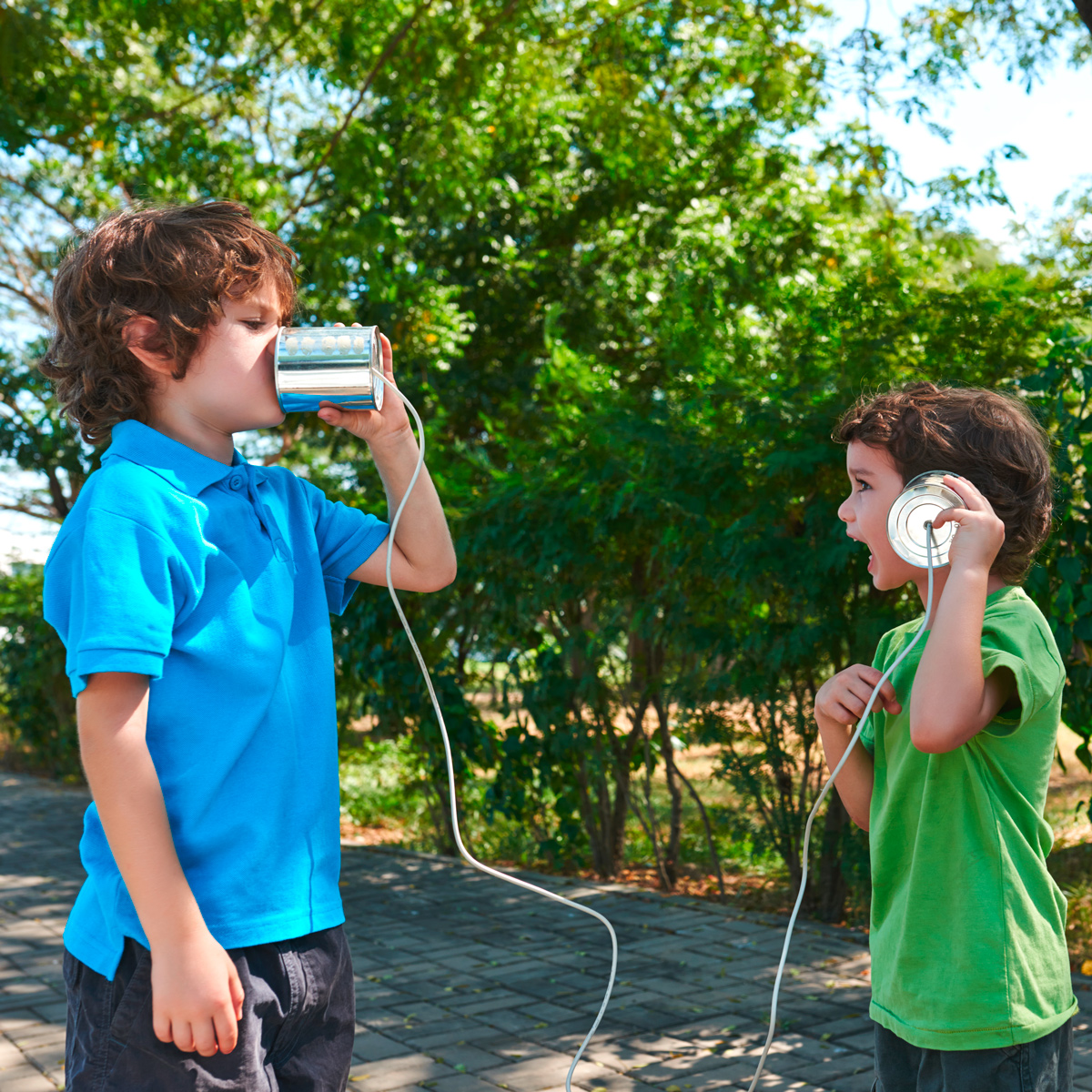 Zwei Kinder spielen draußen mit einem Dosentelefon ©istock/DragonImages
